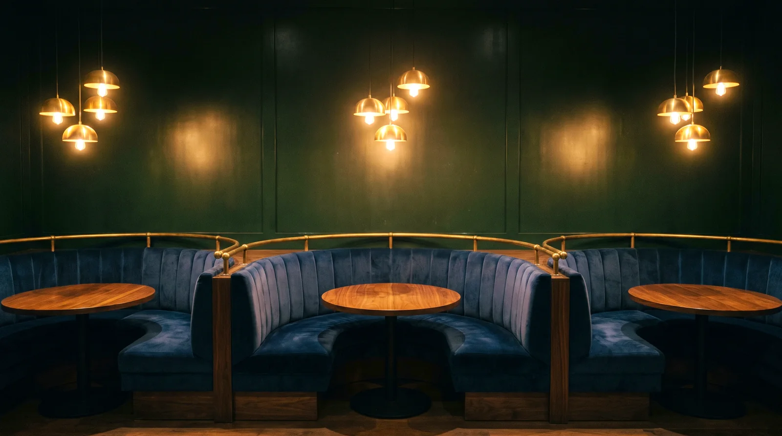 Three U-shaped booths in navy velvet under brass pendants in a hotel restaurant