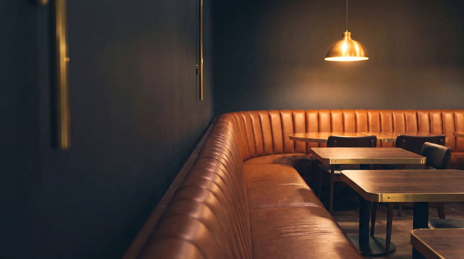 A curved channel-back banquette in cognac leather in a restaurant after closing