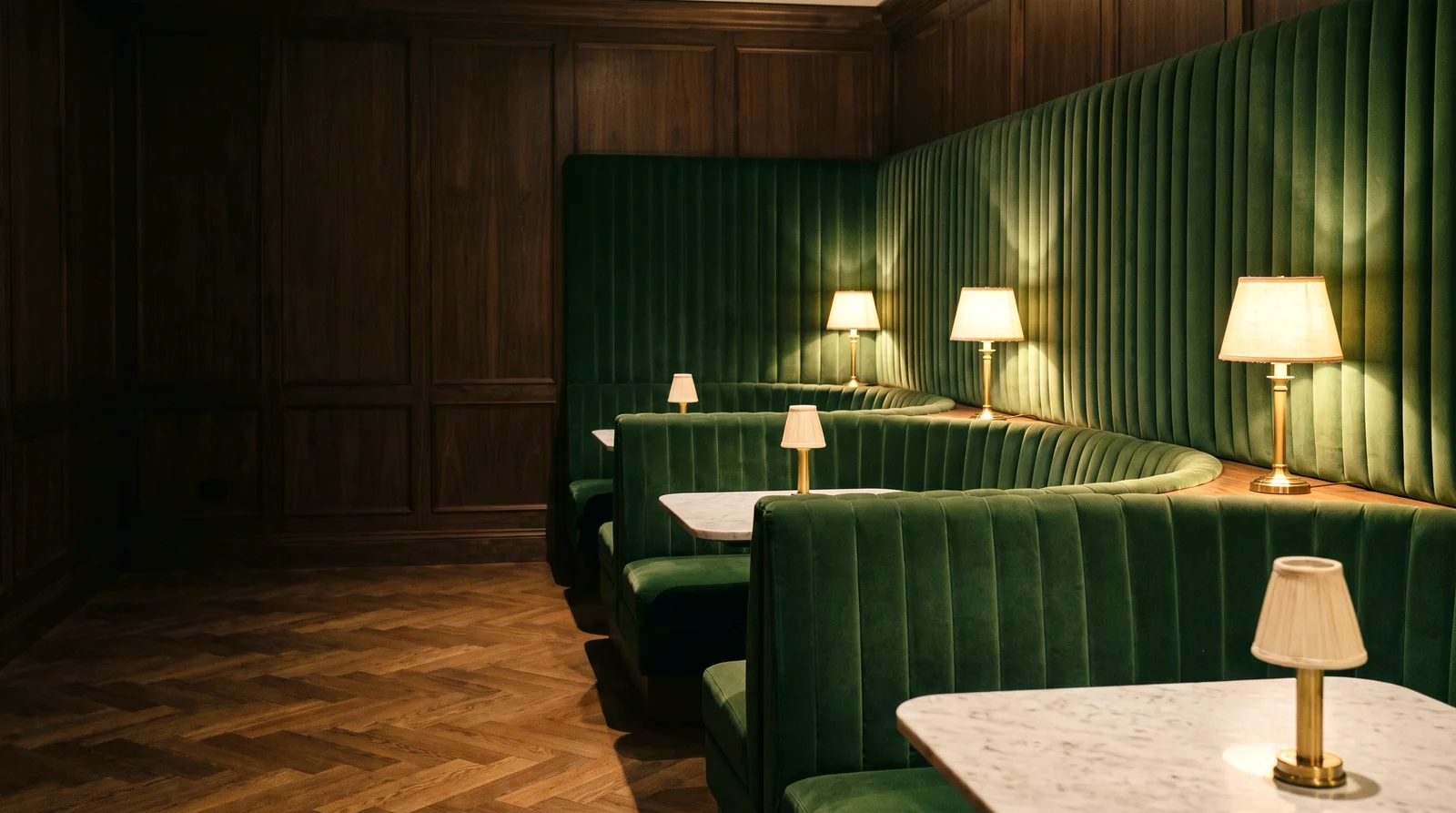 A curved green velvet channel-back banquette in a walnut-paneled members club