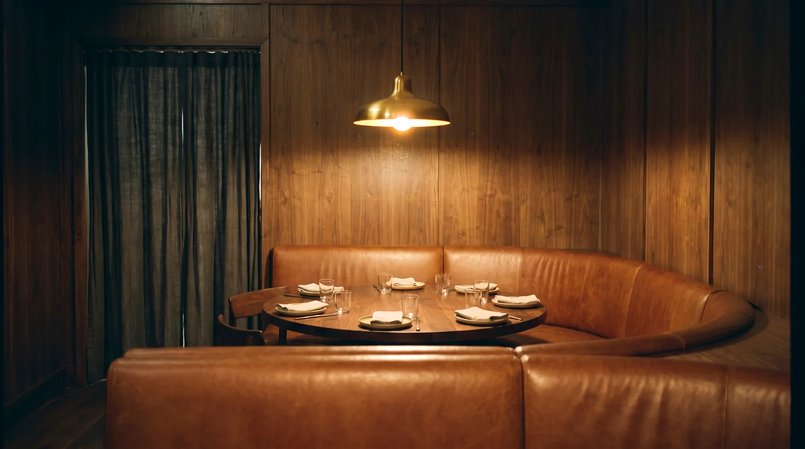 A U-shaped cognac leather booth around a round walnut table in a private dining room