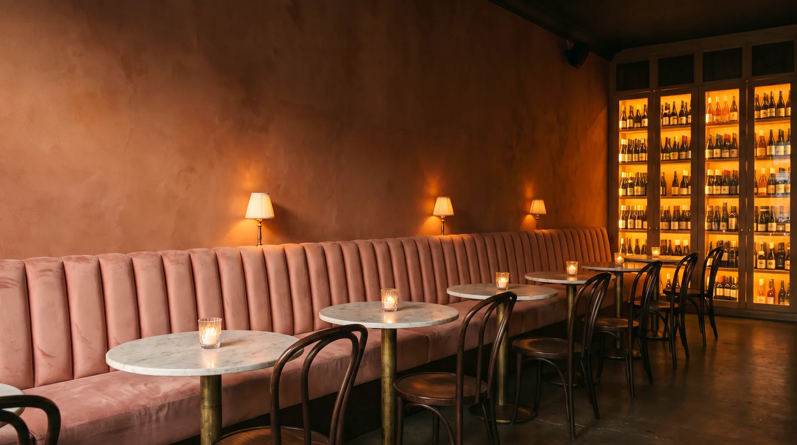 A blush velvet channel-back banquette against a terracotta wall in a wine bar